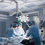 Male surgeon holding instrument in abdomen of patient. Female and male assistants help him. Indian surgeon performing laparoscopic surgery in operating room. Minimally invasive surgery. Blue filter